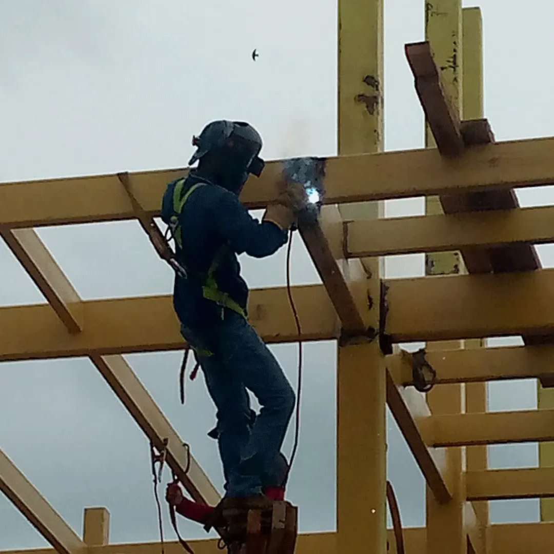 Welder tied off in a harness on a yellow steel structure